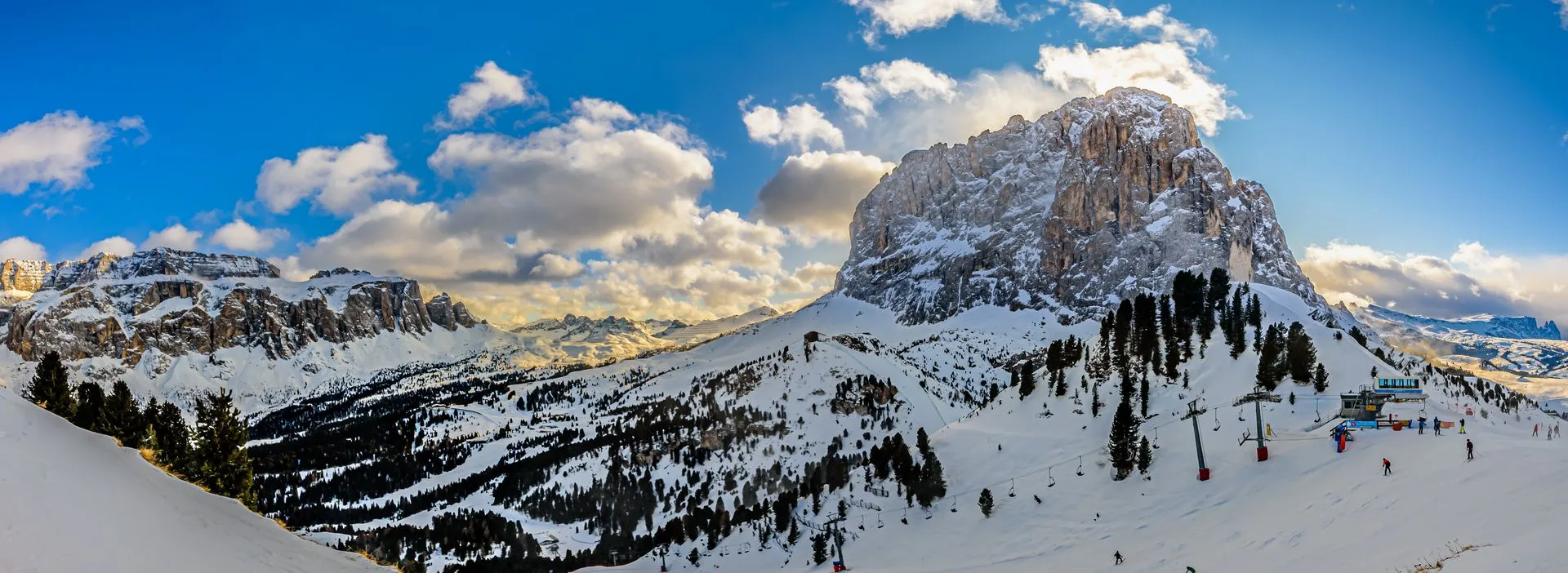 Verschneite Dolomitengipfel über einem Skigebiet mit Sessellift und Wintersportlern im Vordergrund