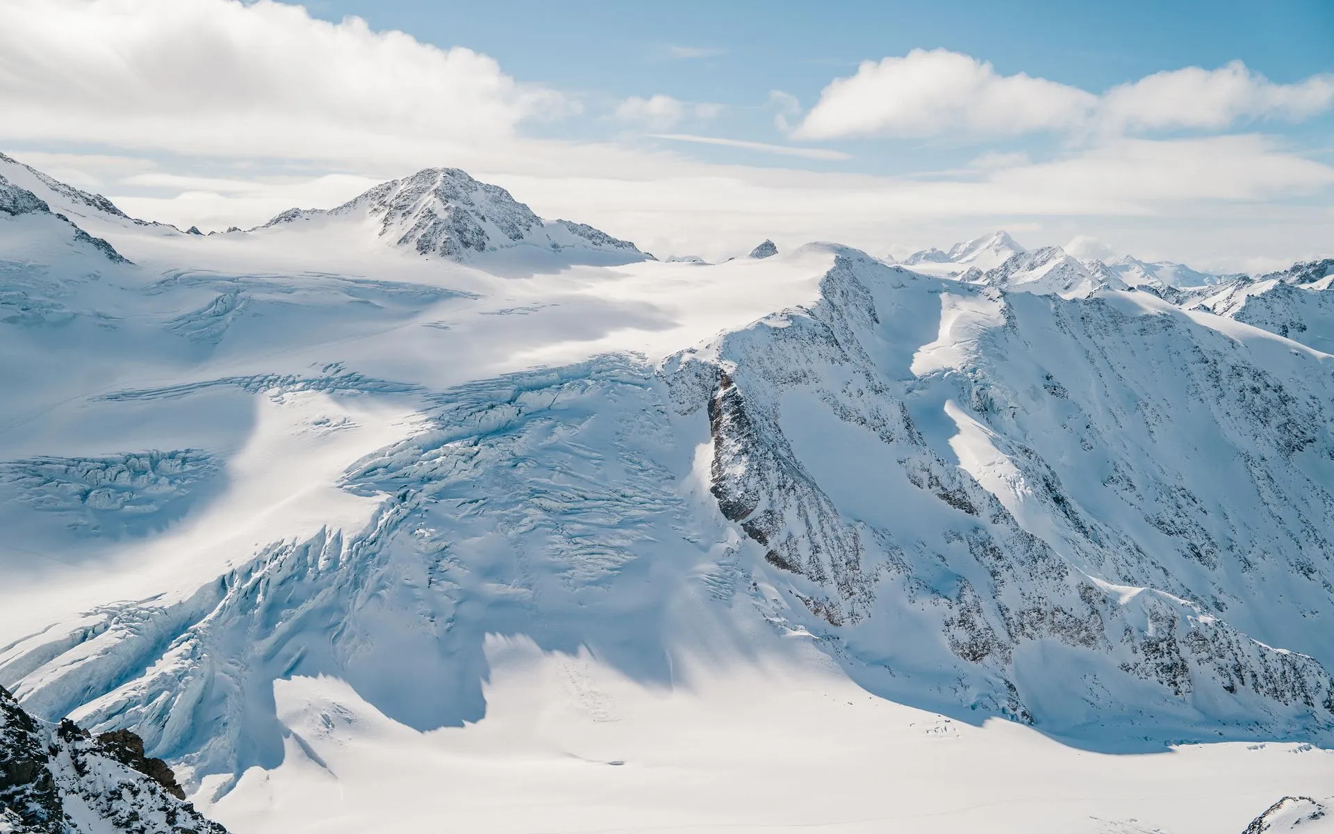 Weite Gletscherlandschaft mit Spalten und schneebedeckten Gipfeln unter blauem Himmel