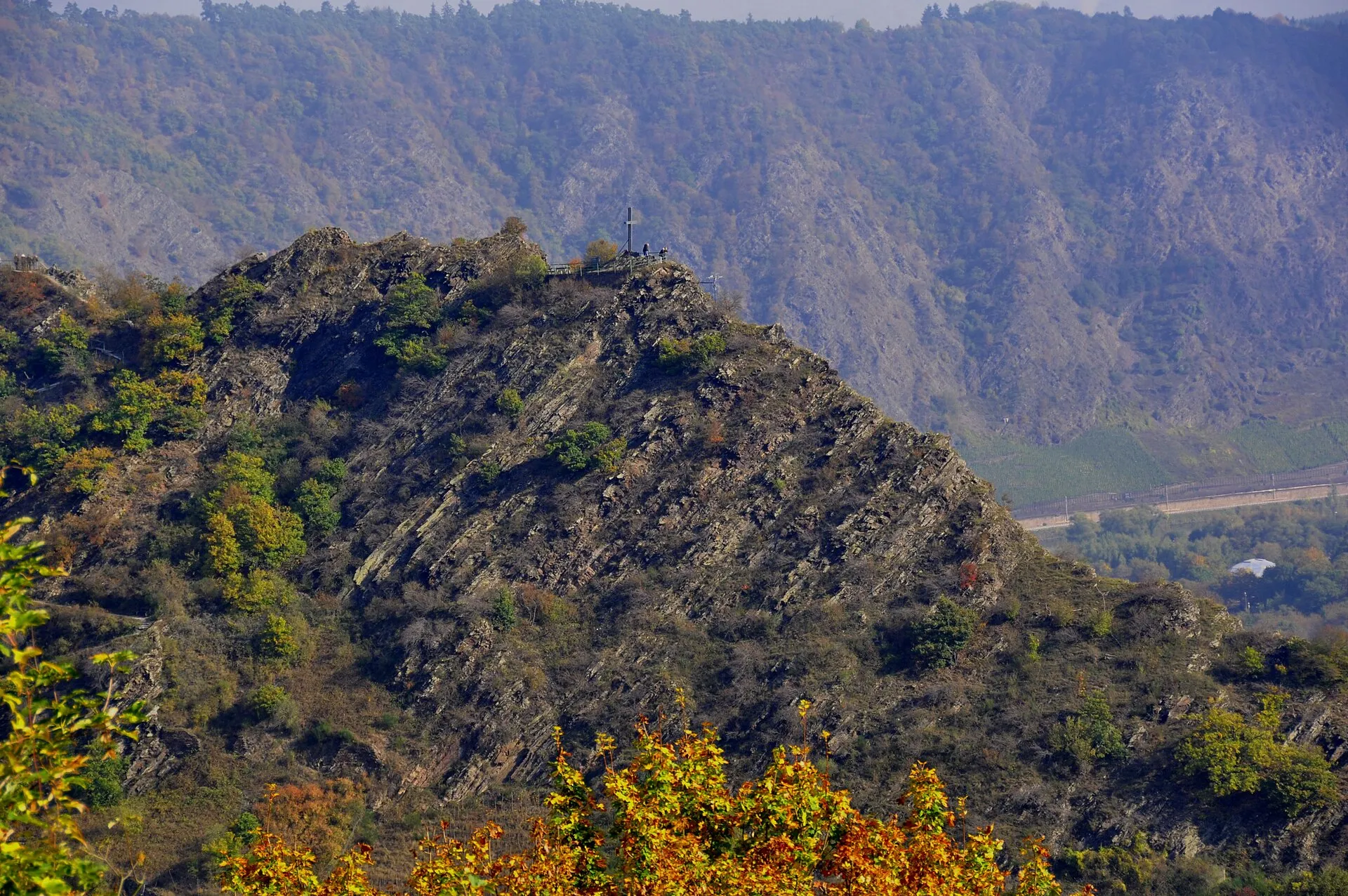Felsgrat des Pinnerbergs über dem Moseltal mit Gipfelkreuz und Aussichtsplattform, ringsum herbstlich gefärbte Hänge