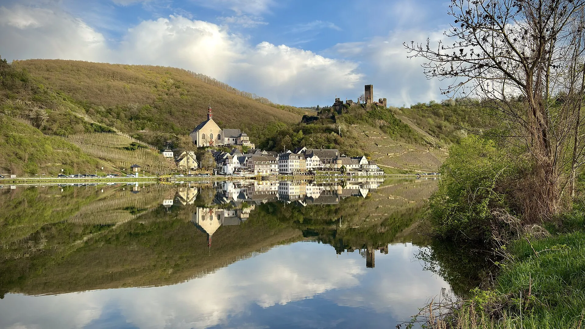 Beilstein vom gegenüberliegenden Moselufer: Klosterkirche, Häuserzeile am Wasser, darüber die Burgruine Metternich