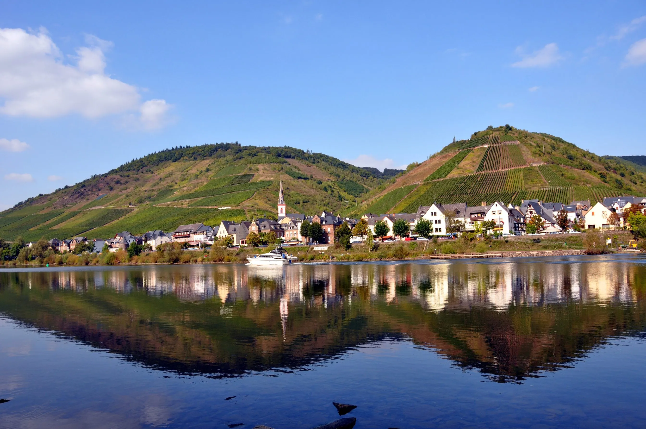 Ediger an der Mosel vom gegenüberliegenden Ufer, Häuserzeile am Wasser vor steilen Weinbergen, davor die Spiegelung