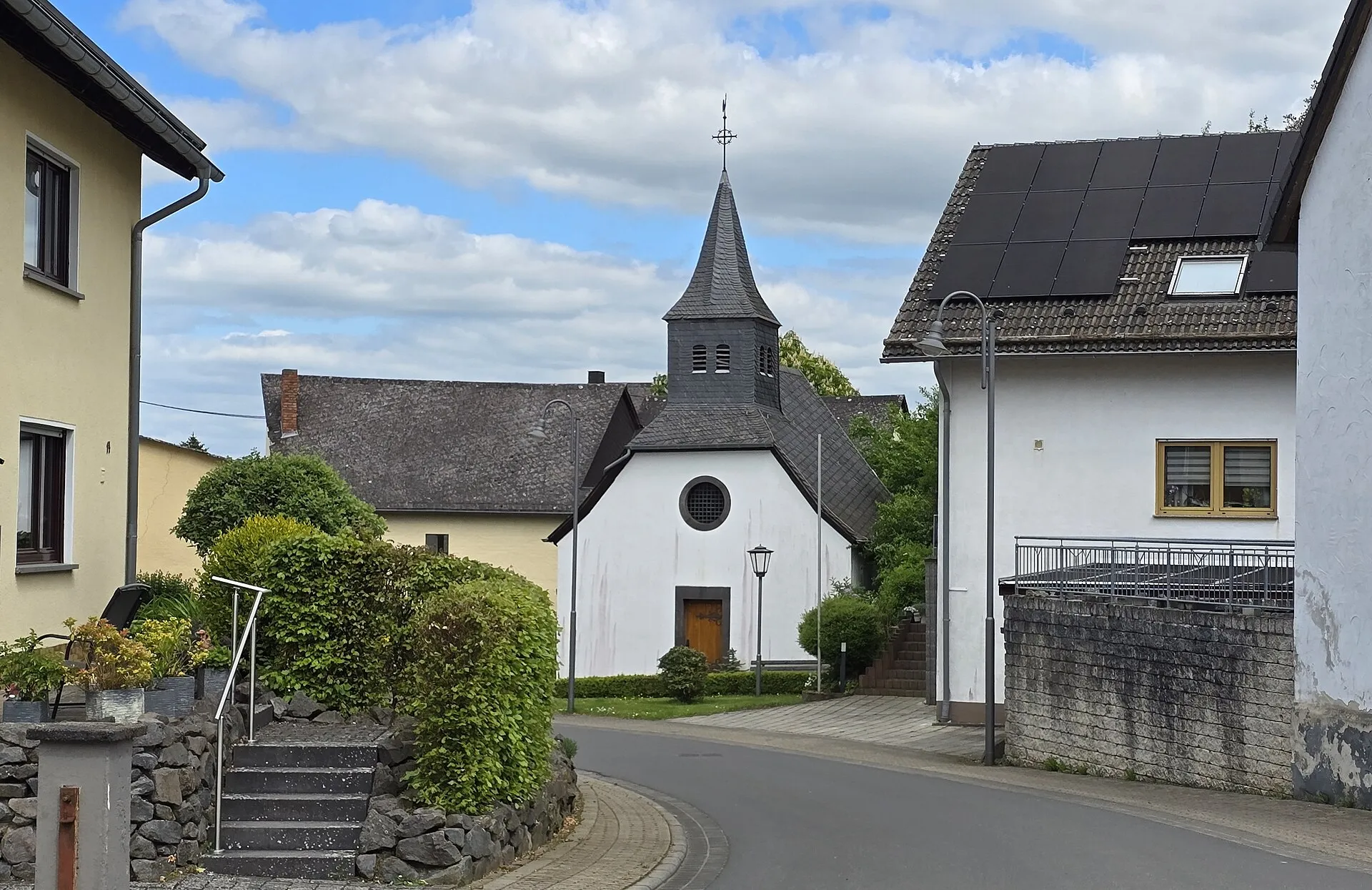 Kirchstraße mit weiß verputzter Saalkirche und schiefergedecktem Dachreiter, links und rechts Wohnhäuser