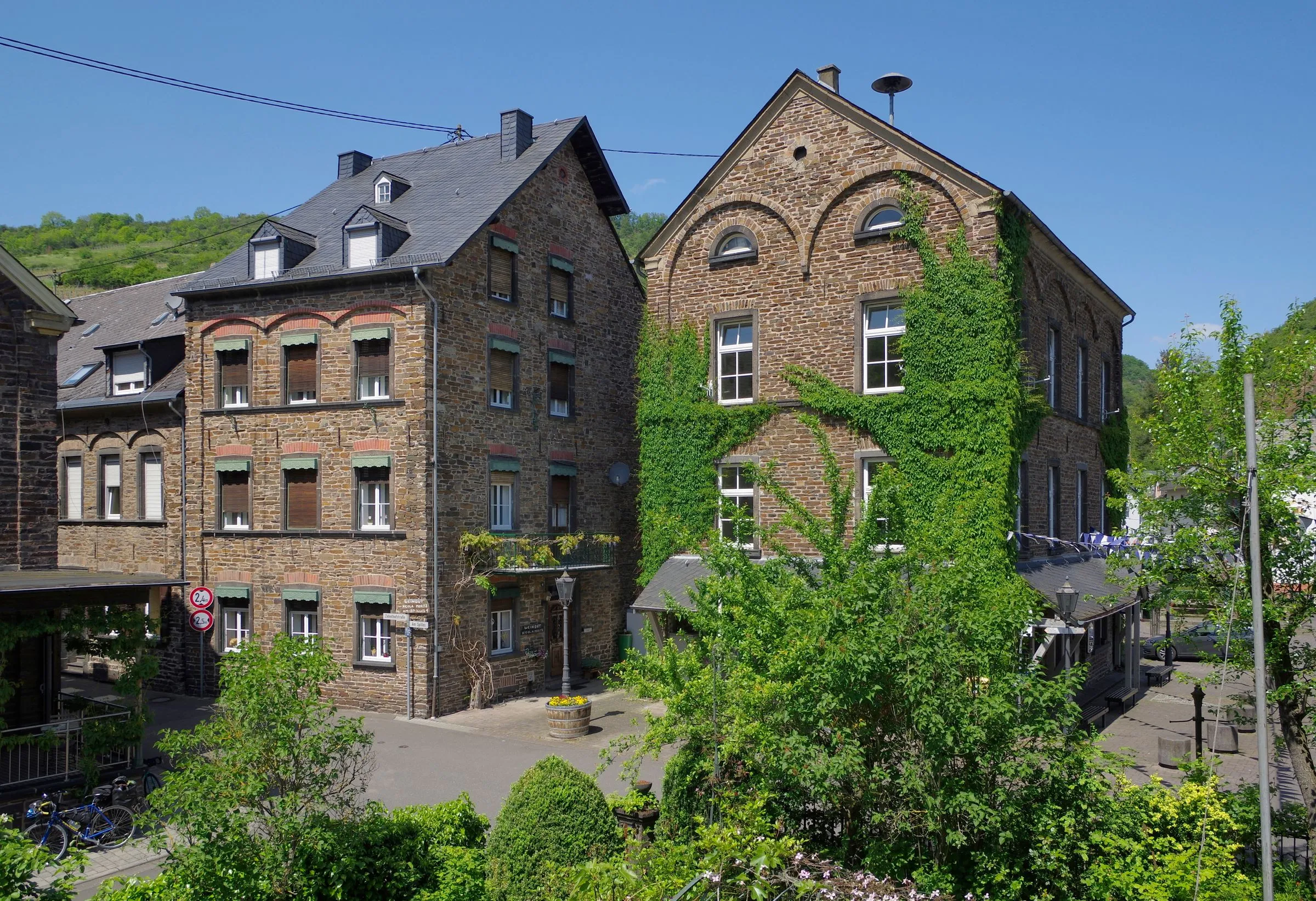 Platz Am Spilles in Pommern mit efeubewachsener alter Schule, Bruchsteinhaus und Wimpelkette über einem Vordach