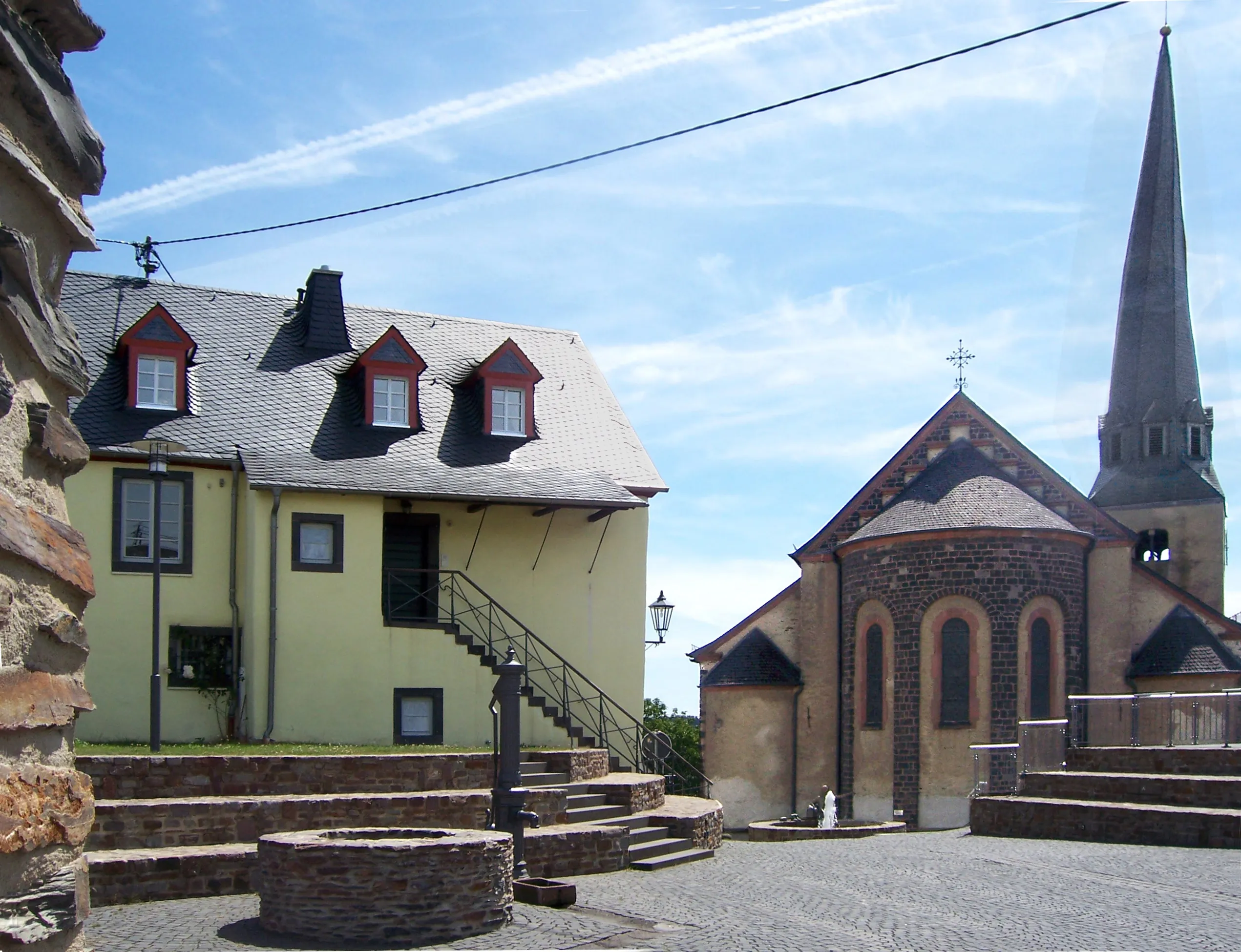Historischer Ortskern von Kaisersesch: gepflasterter Platz mit Brunnen, links ein Haus mit Schieferdach, rechts eine Kirche