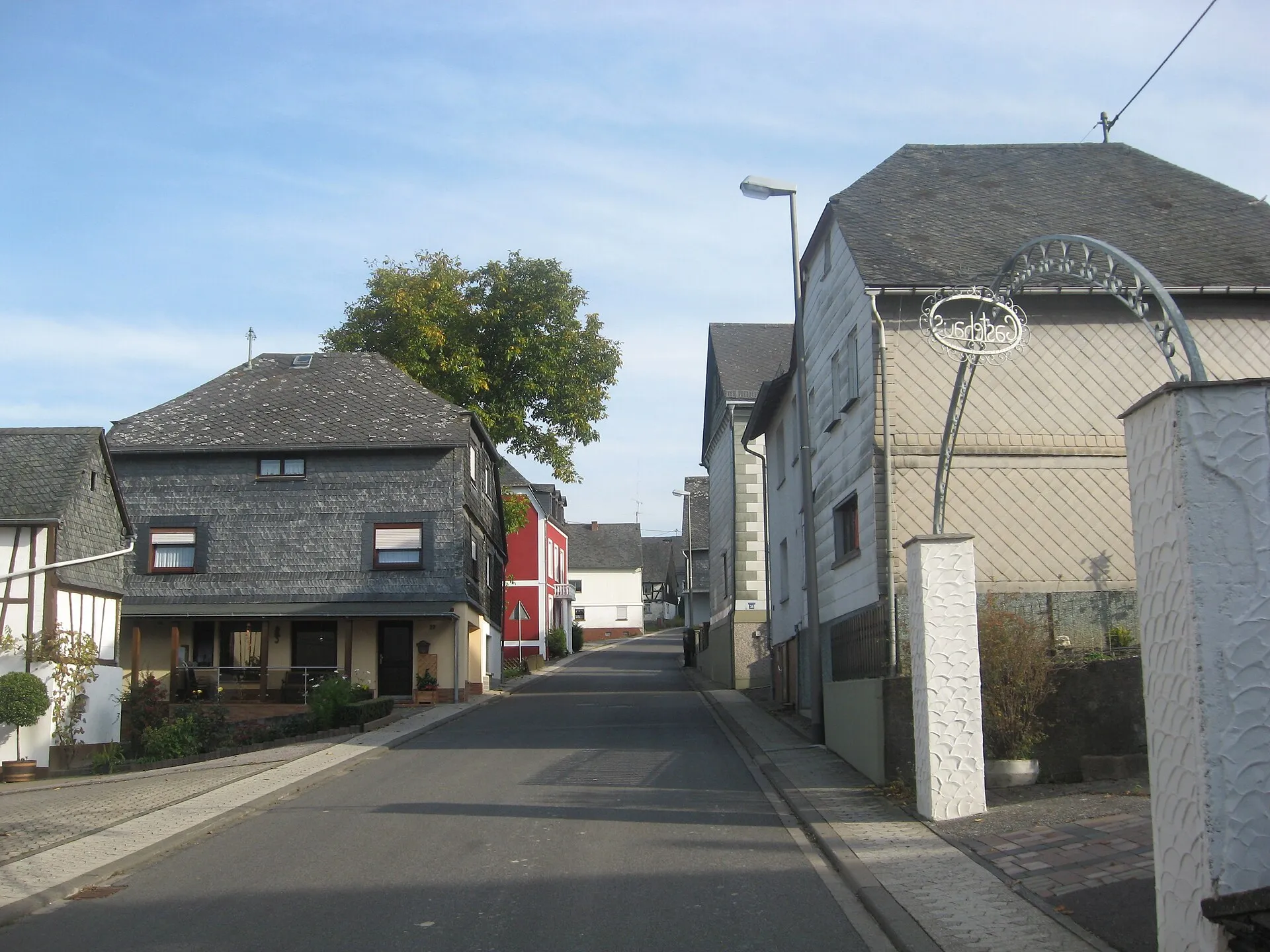 Dorfstraße in Altlay mit schiefergedeckten Wohnhäusern und einem schmiedeeisernen Gasthausschild am rechten Bildrand