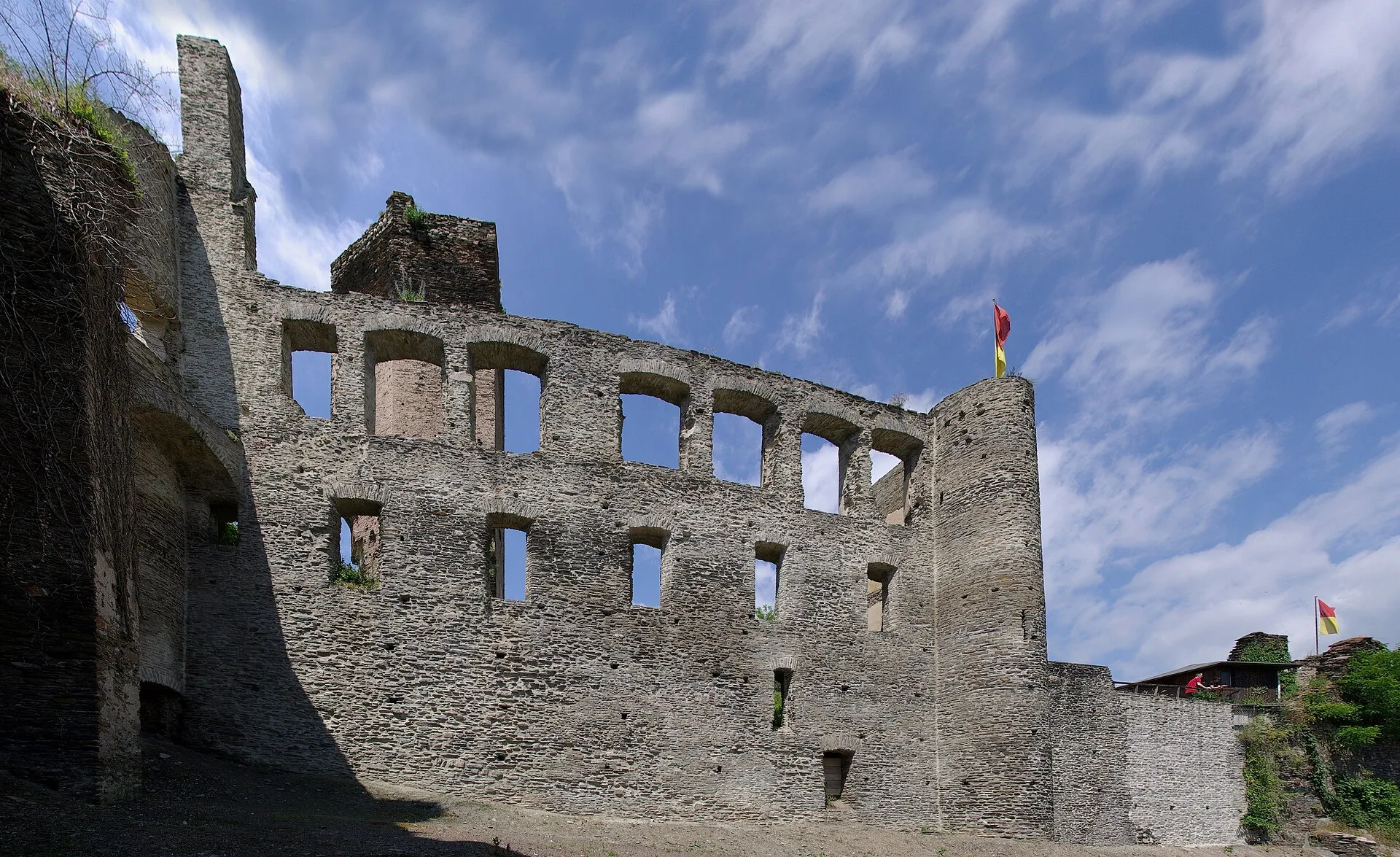 Hohe Ruinenmauer mit zwei Reihen leerer Fensteröffnungen und einem Rundturm an der Ecke, darüber bewölkter Himmel