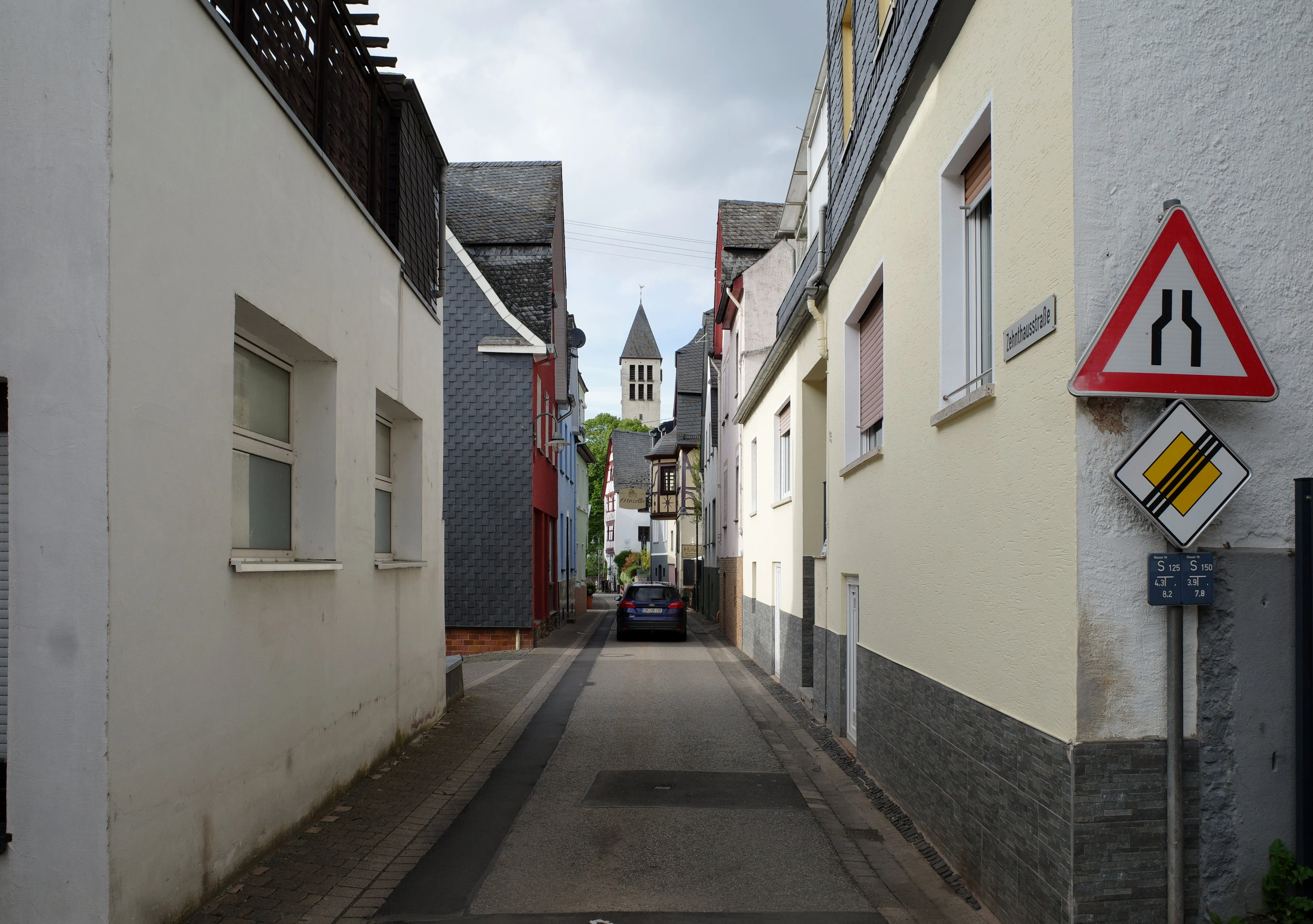 Enge Gasse zwischen verputzten und verschieferten Häusern, am Ende ein freistehender Kirchturm
