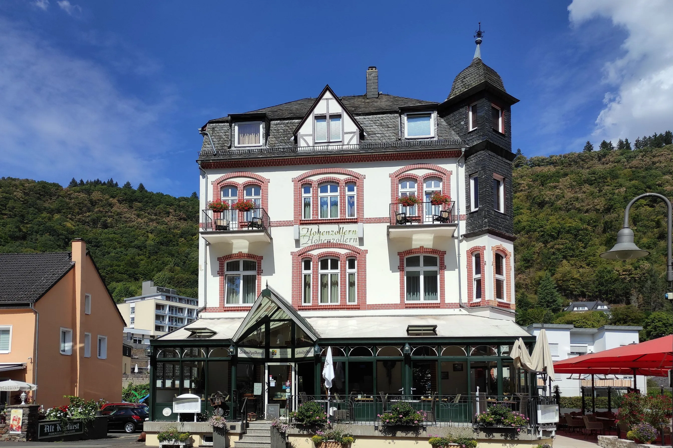 Hotelgebäude mit Ecktürmchen und gläsernem Wintergarten an der Kurfürstenstraße in Bad Bertrich, dahinter ein bewaldeter Hang