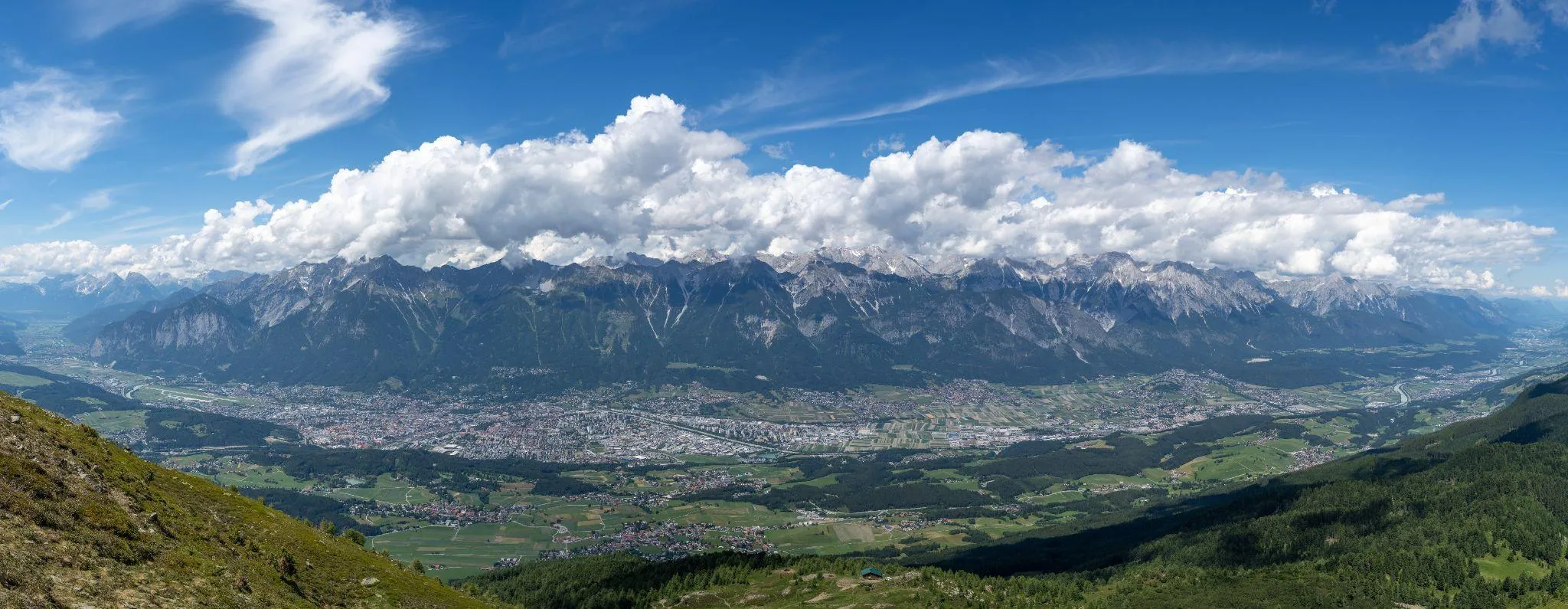 Panorama über das Inntal mit der Stadt Innsbruck im Talboden, dahinter die Felswand der Nordkette unter Wolken
