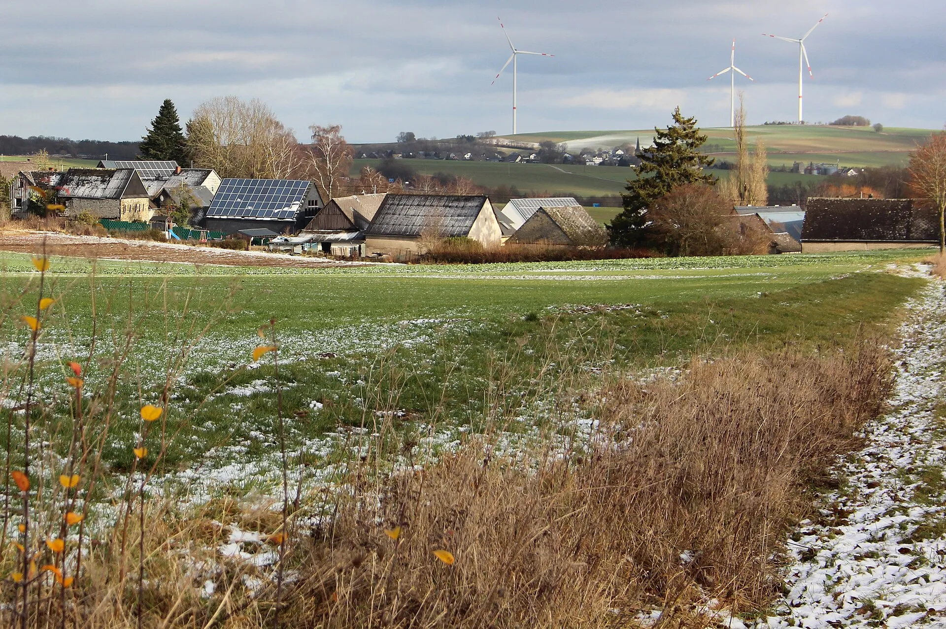 Blick über verschneite Felder auf die Häuser von Zettingen, dahinter Windräder auf dem Höhenrücken