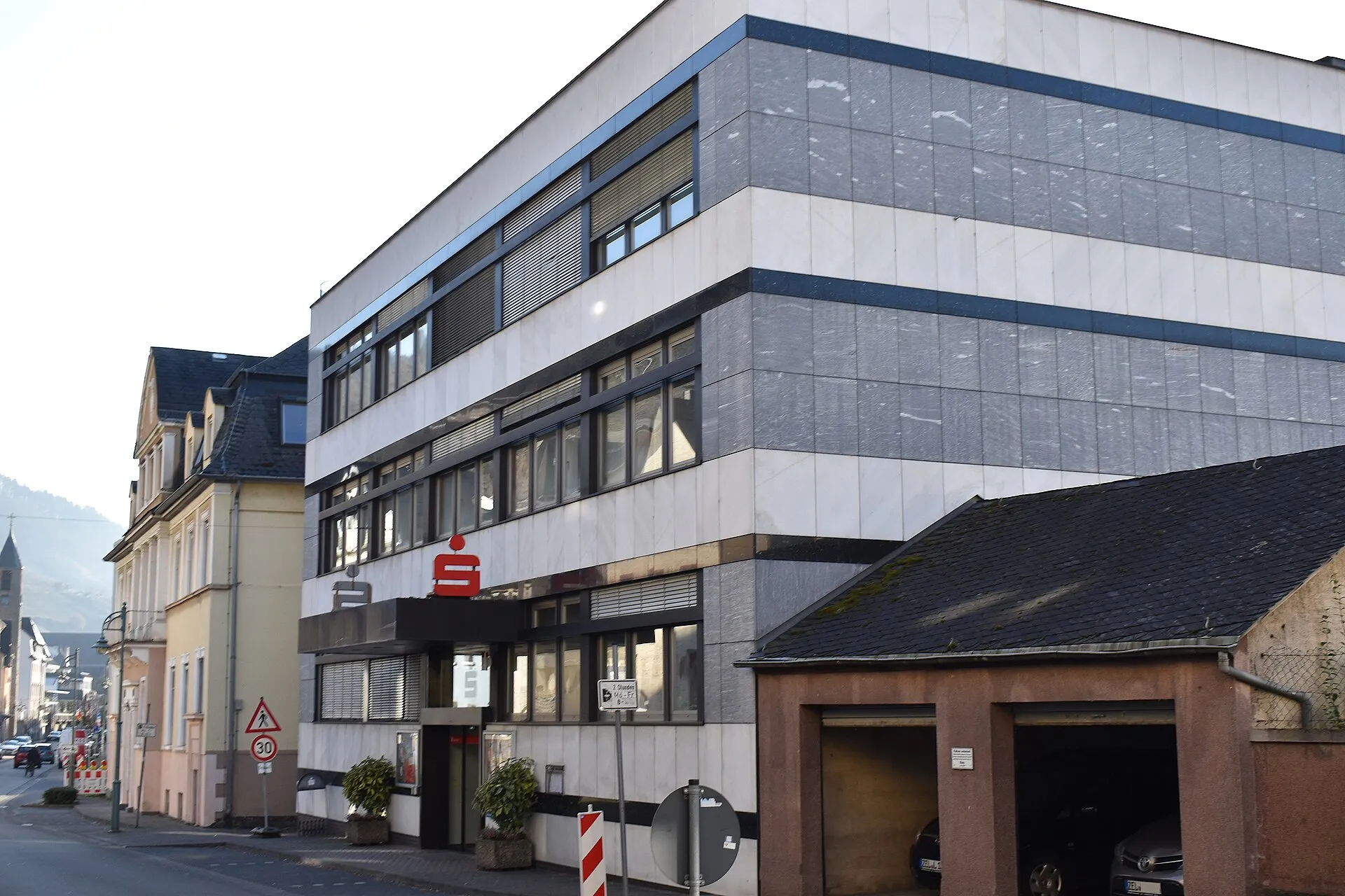 Mehrgeschossiges Bankgebäude mit grauer Plattenfassade an einer Straßenecke, über dem Eingang das rote S-Zeichen