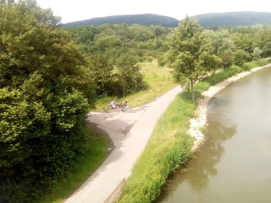 Asphaltierter Radweg am Flussufer, zwei abgestellte Reisefahrräder am Wegrand, dahinter bewaldete Hänge