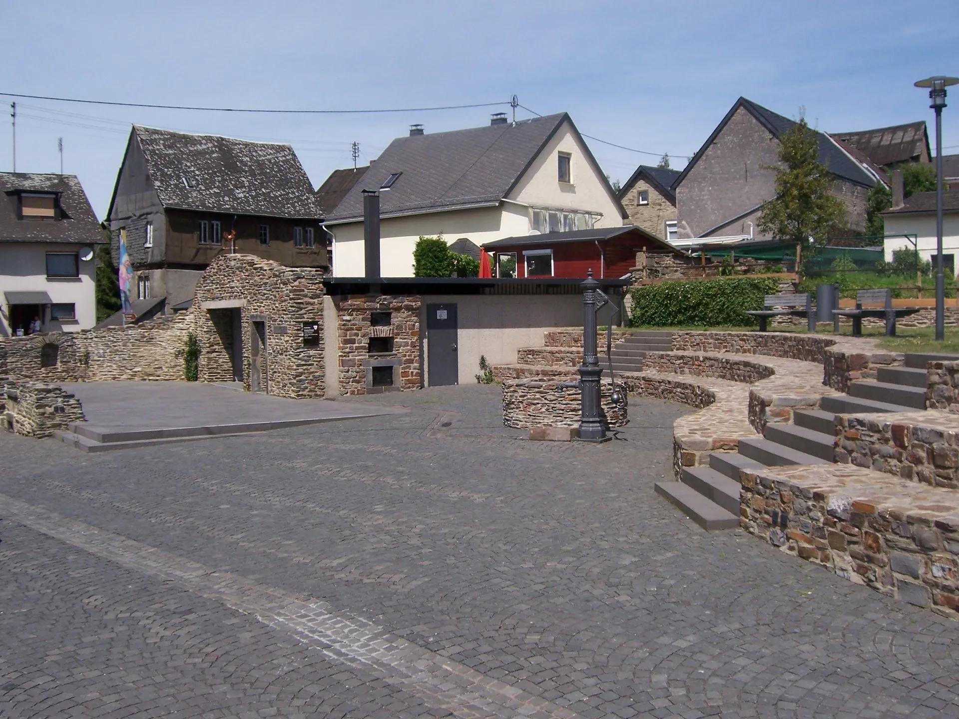 Gepflasterter Platz im historischen Ortskern von Kaisersesch mit Bruchsteinmauern, Treppenstufen und einer alten Handpumpe