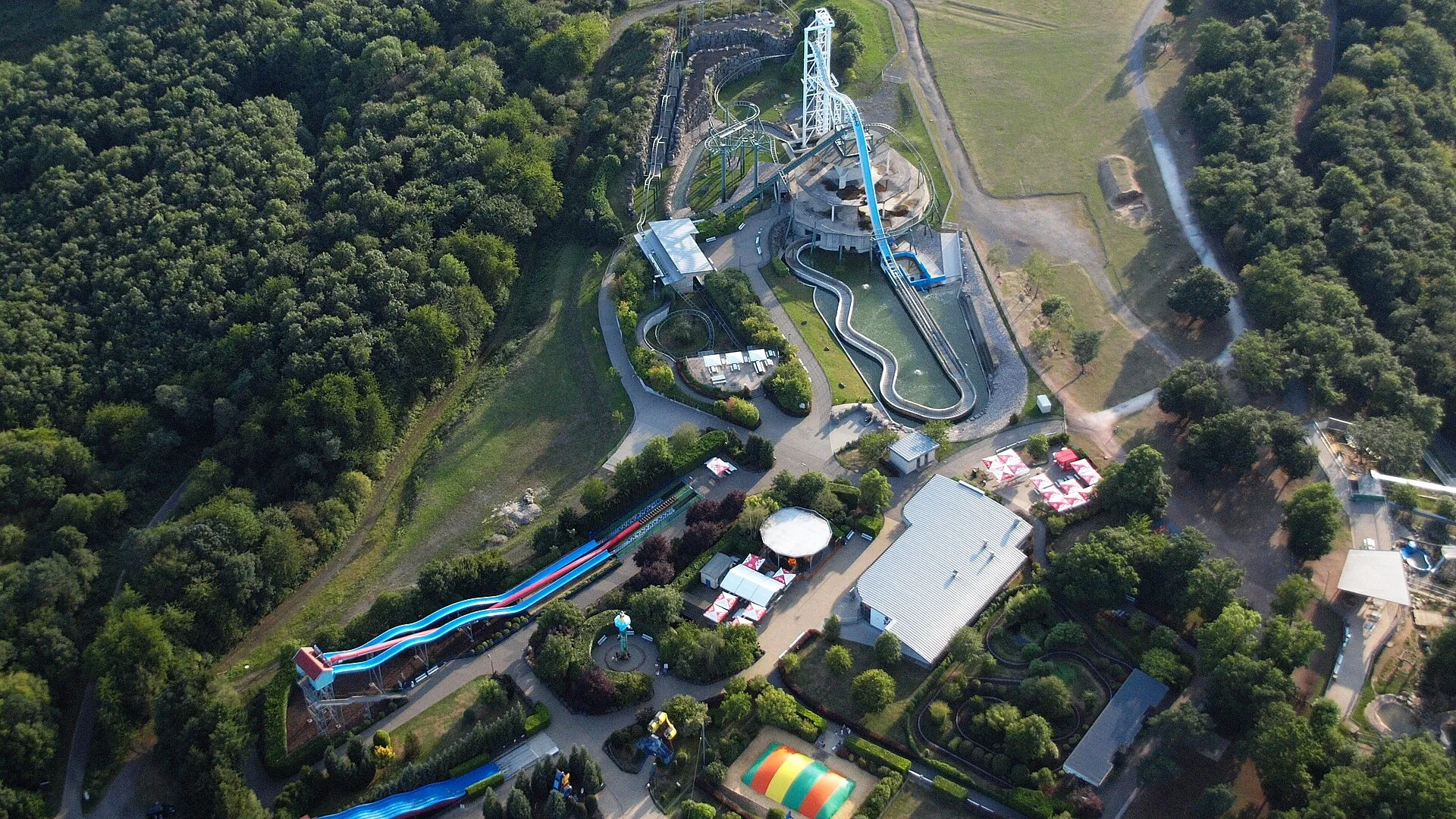 Luftaufnahme eines Freizeitparks auf einer bewaldeten Höhe: Wildwasserbahn, Achterbahn und Rutschen zwischen Bäumen