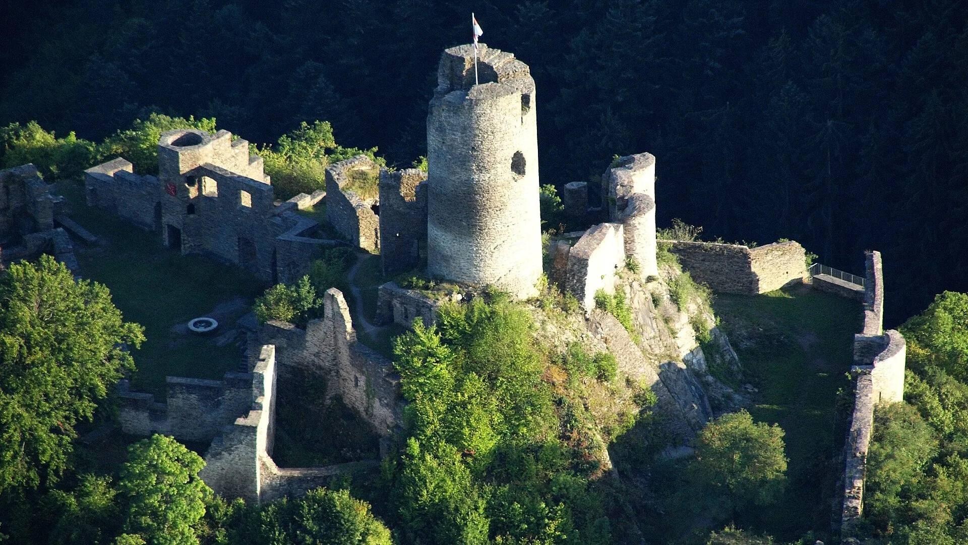 Luftbild der Burgruine Winneburg mit rundem Bergfried und Mauerresten auf einem bewaldeten Bergsporn