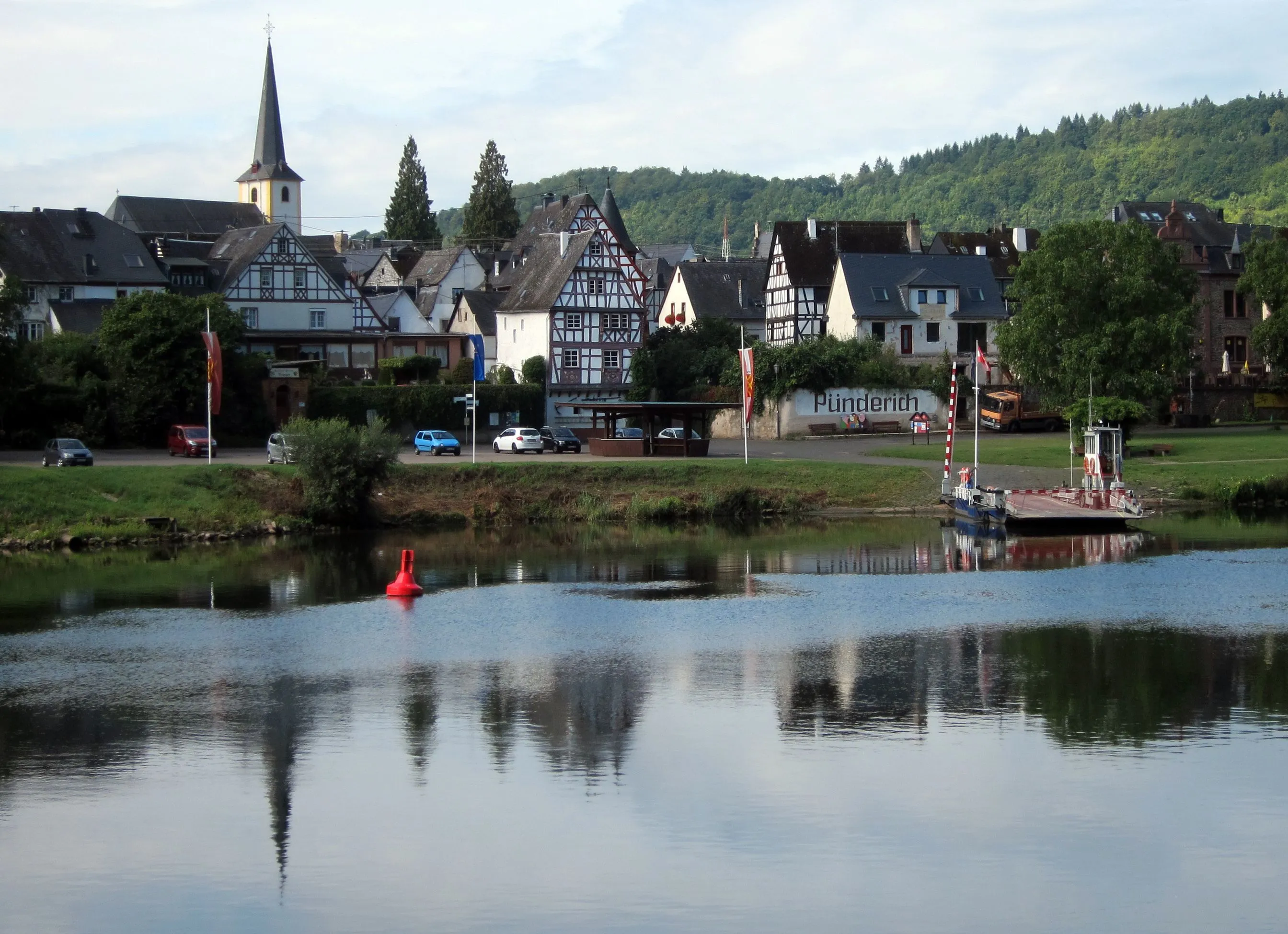 Blick über die Mosel auf Pünderich mit Fachwerkhäusern, Kirchturm und der Fähre am Ufer