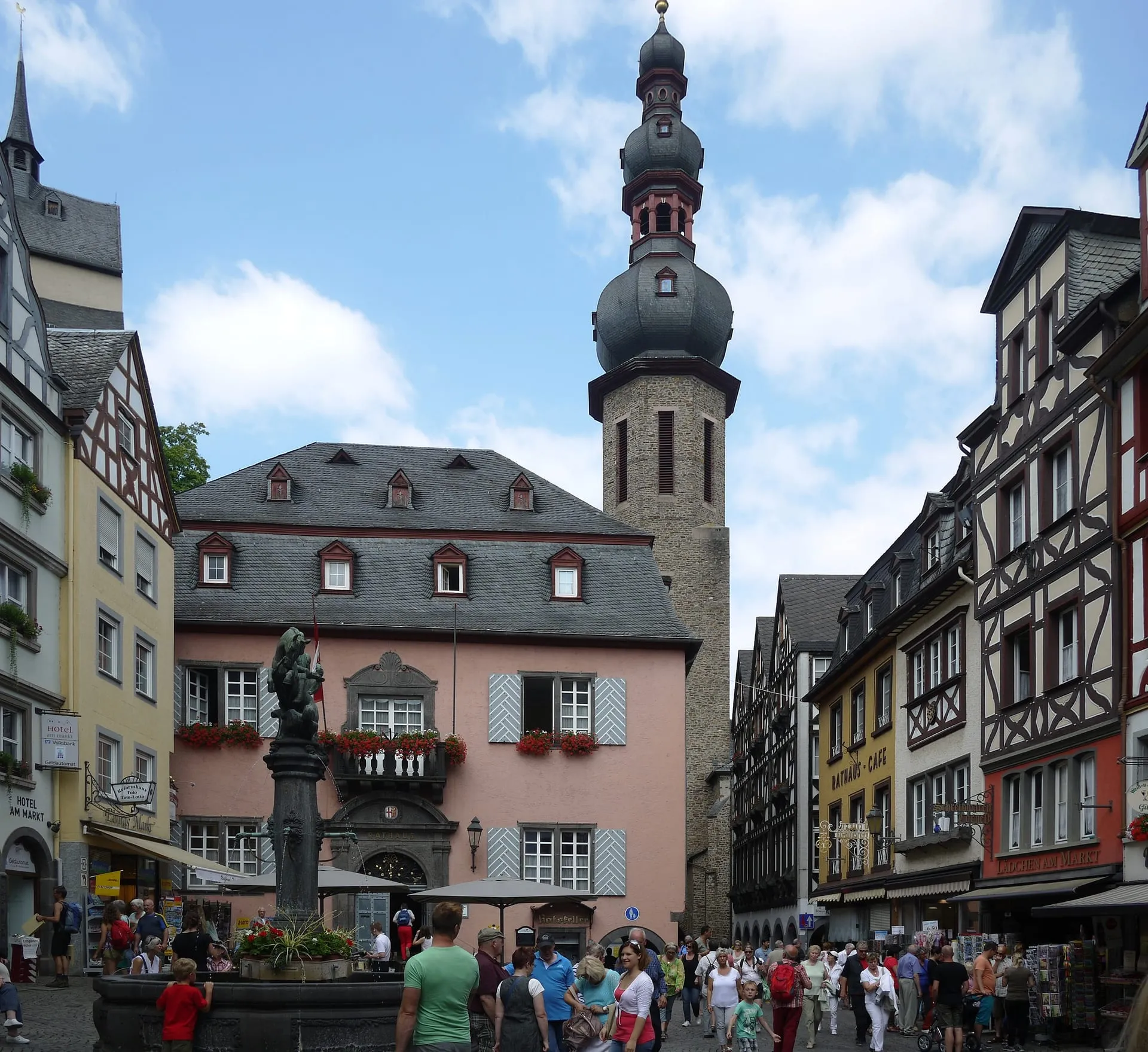 Sonniger Marktplatz in Cochem mit rosa Rathaus, Zwiebelturm von St. Martin und Fachwerkhäusern