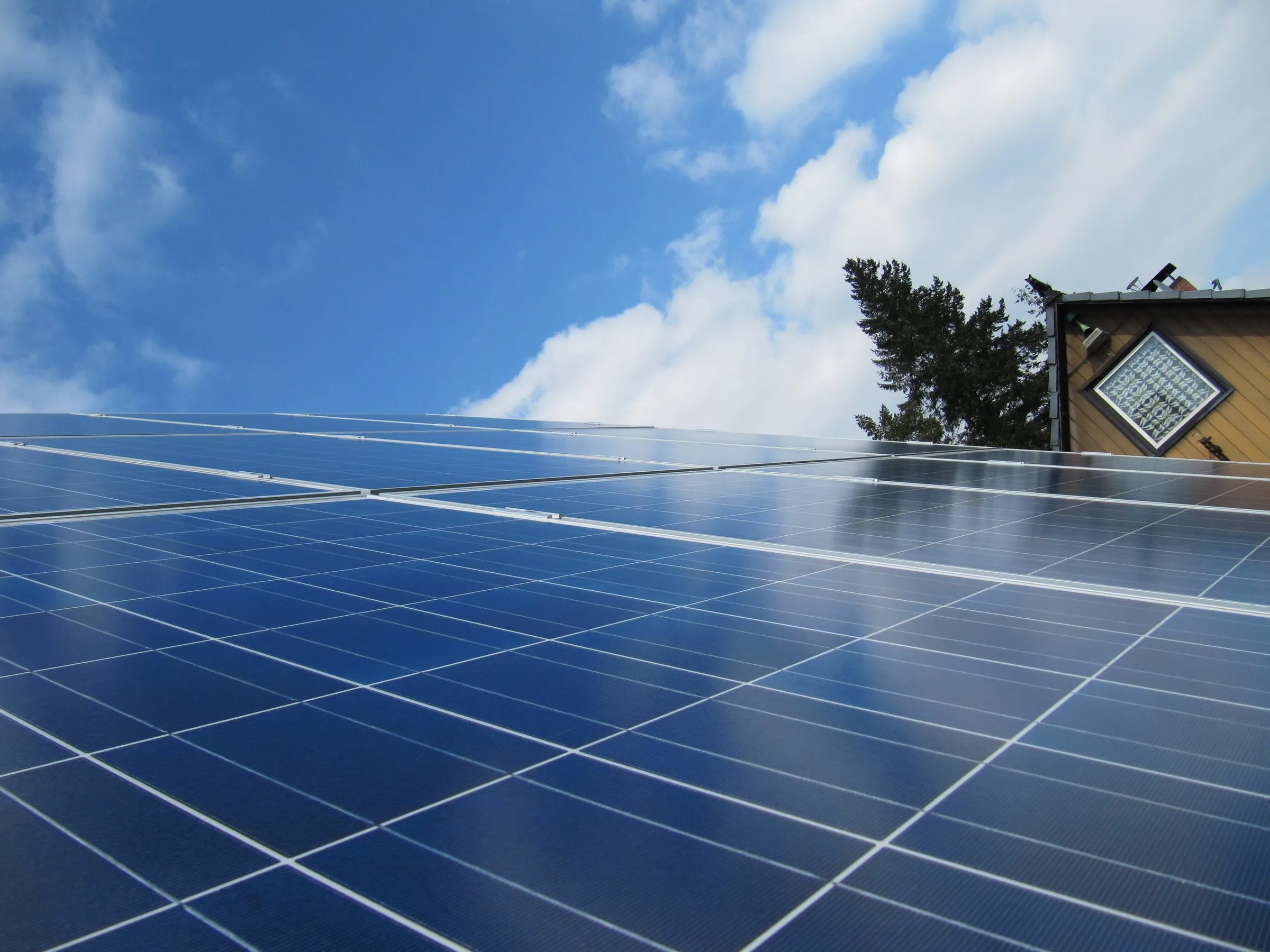 Blick über eine Reihe blauer Solarmodule auf einem Hausdach gegen blauen Himmel mit Schönwetterwolken