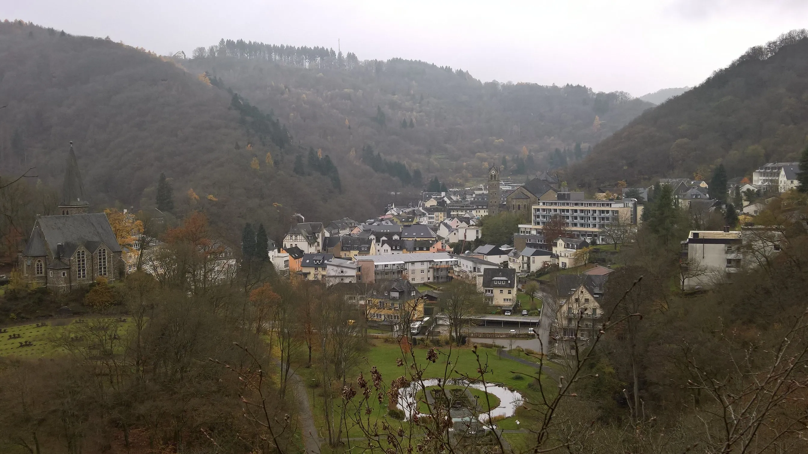 Blick von einem Hang hinunter auf Bad Bertrich im engen Üßbachtal, im Vordergrund ein Weiher in einer Parkanlage