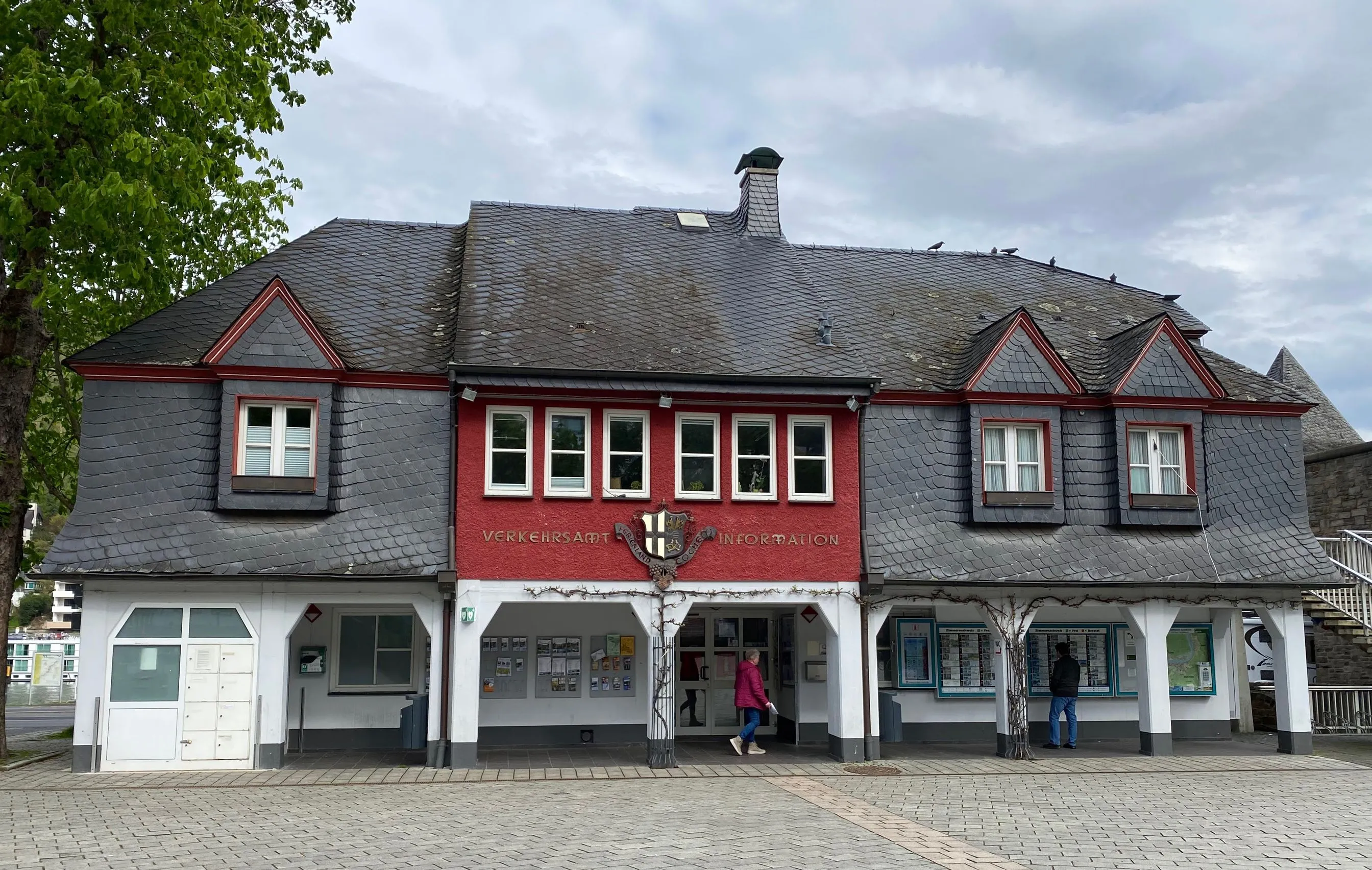 Das Gebäude des Verkehrsamts Ferienland Cochem mit roter Fassade und Schieferdach am leeren Endertplatz in Cochem