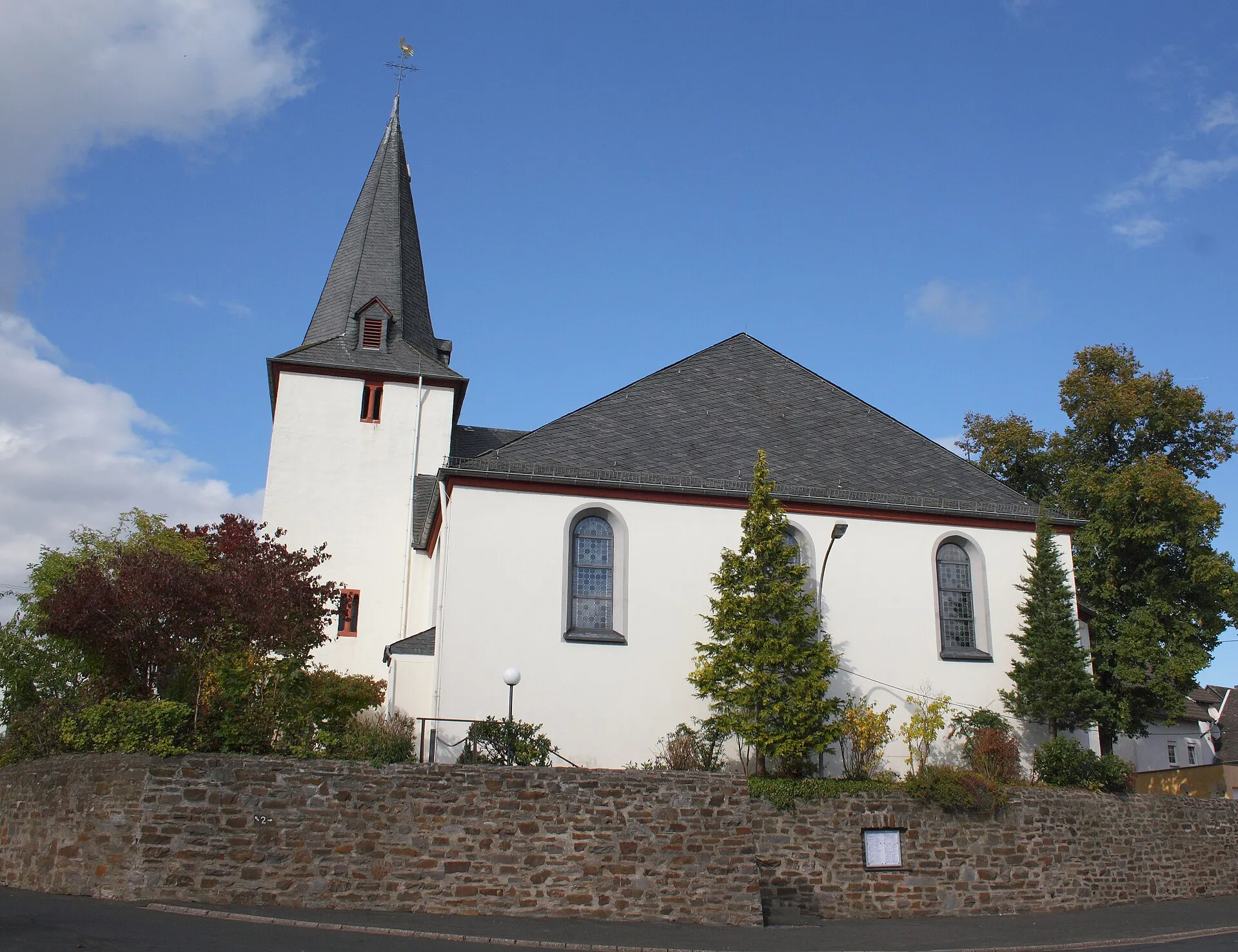 Die weiß verputzte Pfarrkirche St. Stephan in Faid mit schiefergedecktem Turmhelm über einer Bruchsteinmauer
