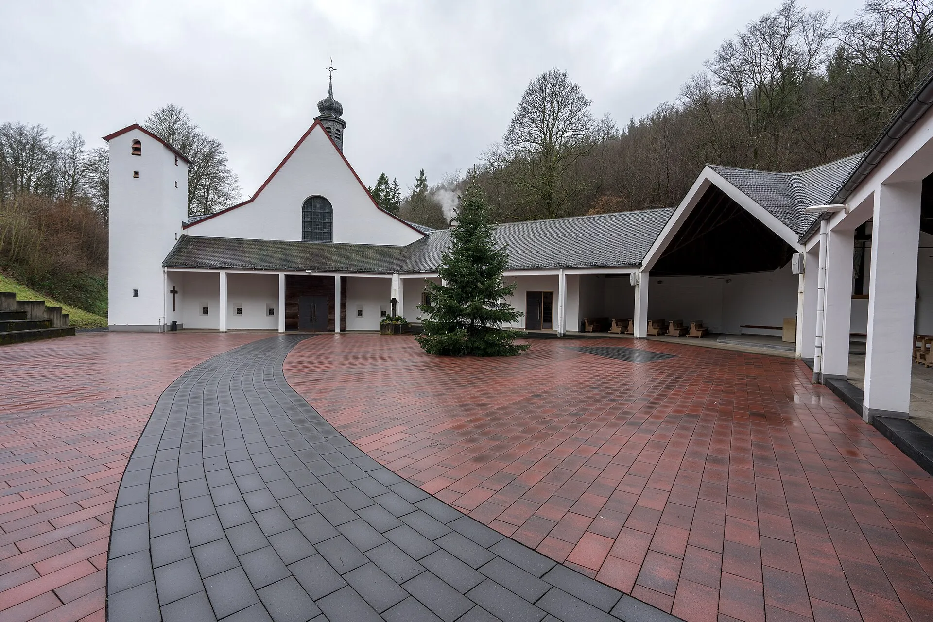 Gepflasterter Kirchplatz vor der weißen Wallfahrtskirche Maria Martental, daneben ein überdachter Freiluftbereich